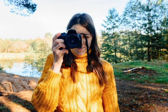Young woman photographer taking photo on the camera in the autumn forest.