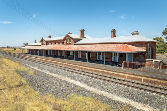 Historic red brick railway station with long platform on flat outback plains