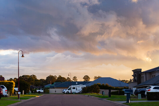 Streetscape in suburban area with clouds overhead and last light on hedge