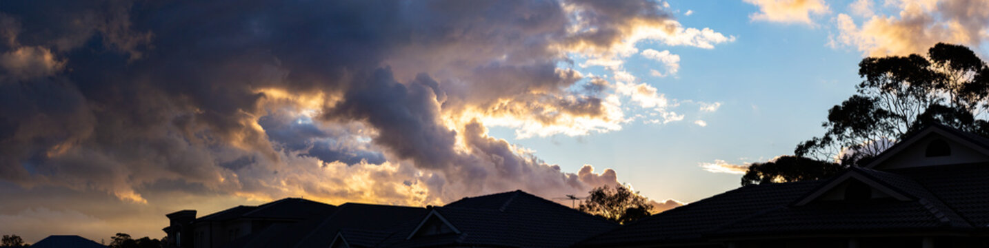 Clouds above rooftops silhouetted against sunset sky
