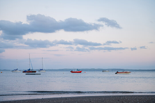 Several boats are anchored in still water as the sun sets