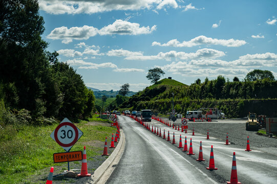 Road work in progress with traffic cones on the side of the road, cars driving slowly