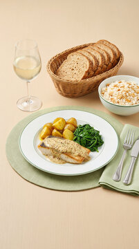 Fish fillet with mustard sauce, roasted potatoes, saut&eacute;ed spinach, rice with almonds, bread, and a glass of white wine