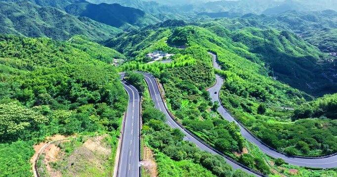 Winding asphalt highway curves through lush green forest mountains in Siming Mountain, Ningbo, under bright daylight.
