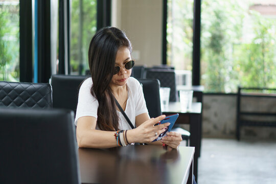 Asian Woman uses smartphone for mobile communication, during relaxation at restaurant cafe table. Digital lifestyle and internet connection concept.