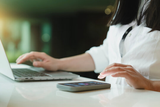 Businesswoman using laptop beside smartphone showing financial dashboard and charts, digital technology for business data analysis, online finance, performance monitoring and office productivity.