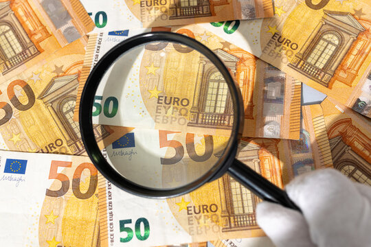 hand holding magnifying glass inspecting euro banknotes. Financial investigation tracing auditing concept