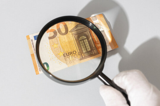 hand holding magnifying glass inspecting a euro banknote. Financial investigation tracing auditing concept