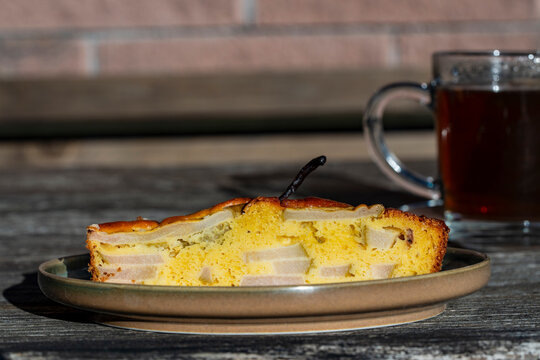 Slice of homemade pear cake on plate with cup of tea, closeup. Fresh slice of delicious pear pie on ceramic plate served with glass cup of hot tea on rustic wooden table