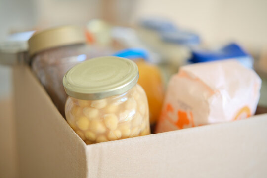 Cardboard box packed with groceries and preserved food jars. Food bank donation and community aid. Grocery collection for families in need. Food assistance and charitable giving.