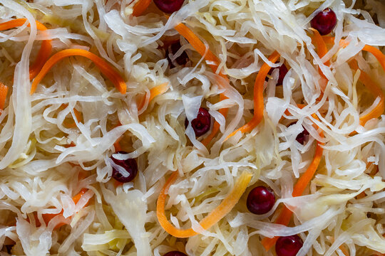 Sauerkraut with carrots and cranberries texture background. Detailed closeup background of traditional fermented sauerkraut mixed with shredded carrots and red cranberries