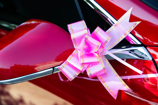 Pink ribbon bow with gold trim on red car side mirror, wedding car decoration, closeup view