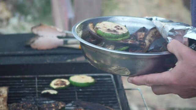 Vegetables grilling outdoors, person cooking zucchini slices and eggplant on charcoal barbecue. Static close-up shot.