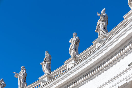 Stone statues of saints on the colonnade of St. Peter's Square against a deep blue sky, Vatican, Rome