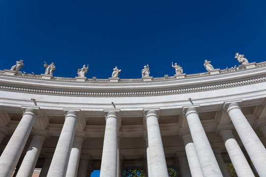 Bernini colonnade with statues of saints against deep blue sky in St. Peter's Square, Vatican City