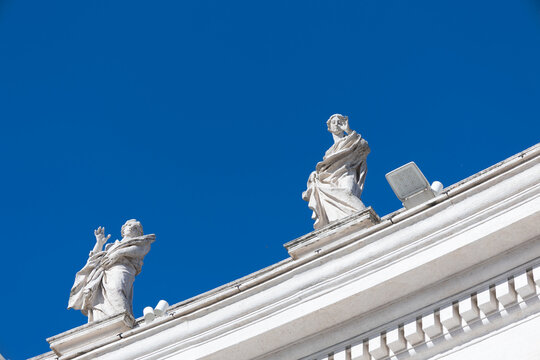 Baroque stone statues on the colonnade roofline of St Peter's Basilica against a deep blue sky, Vatican, Rome