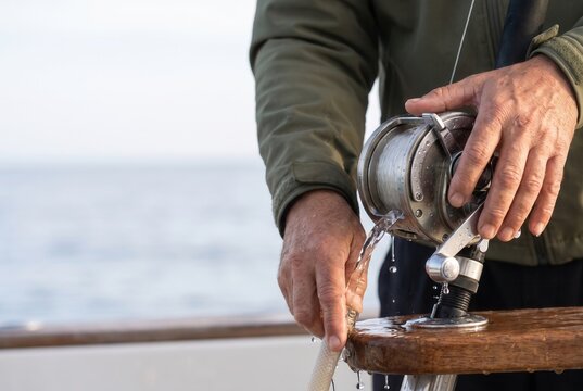Hands cleaning a fishing reel with a cloth