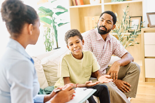 Fatherwith his teenage son boy at meeting with social worker, psychologist discussing mental health family sitting on sofa in psychotherapist office