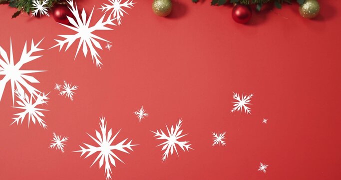 Paper snowflakes and pine sprigs framing red and gold ornaments on crimson surface, copy space