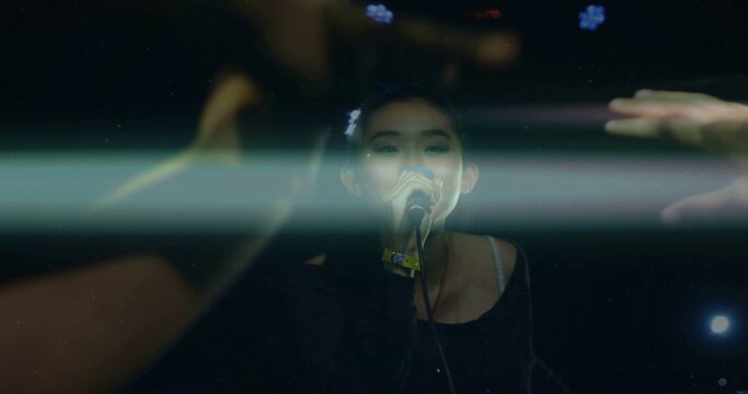 Asian female singer performing into microphone on dark stage with wristband and light beams