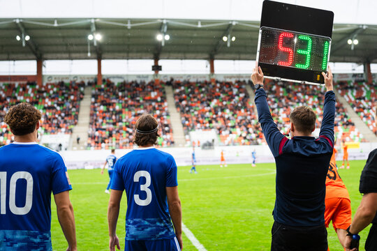 Fourth official holding up a digital electronic substitution board showing player numbers during a professional soccer match.