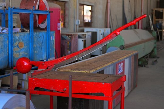 Manual metal guillotine. An antique, red, manually operated guillotine machine designed for cutting metal. A classic, old-style lever-operated cutter.