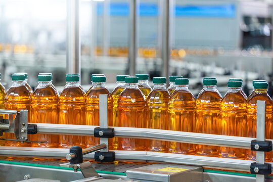 Beverage Bottling and Packaging Manufacturing with Rows of Capped Plastic Bottles Filled with Amber Liquid on Automated Conveyor Inside Modern Factory