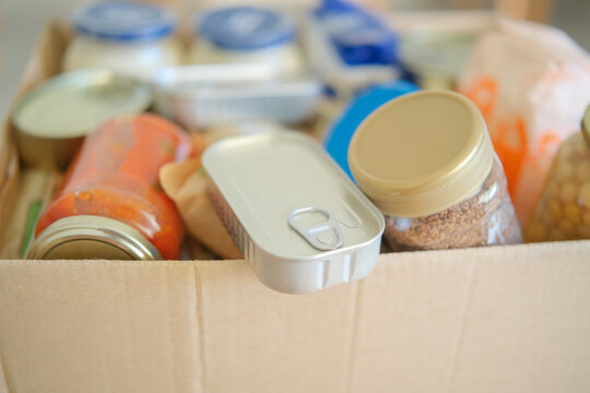 Cardboard box packed with groceries and preserved food jars. Food bank donation and community aid. Grocery collection for families in need. Food assistance and charitable giving.