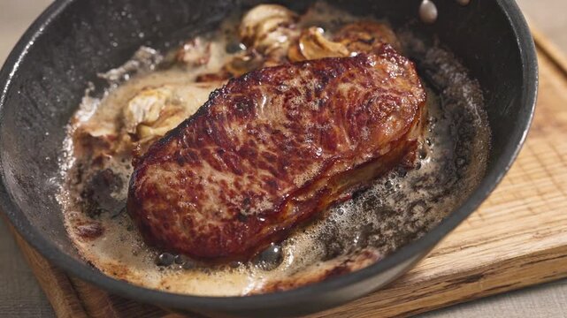 chef pouring melted butter over a juicy beef steak cooking with garlic in a hot pan in the kitchen. The rich butter coats the seared meat, enhancing its flavor and helping create a golden brown crust