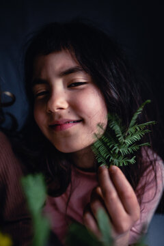 Smiling girl holding a green leafy sprig beside her face