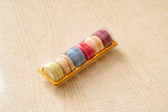 Colorful macarons in a clear gift tray. Six assorted French macarons in pastel shades sit in a plastic display box on a wood surface. Ideal for bakery, confectionery, and gift packaging visuals.