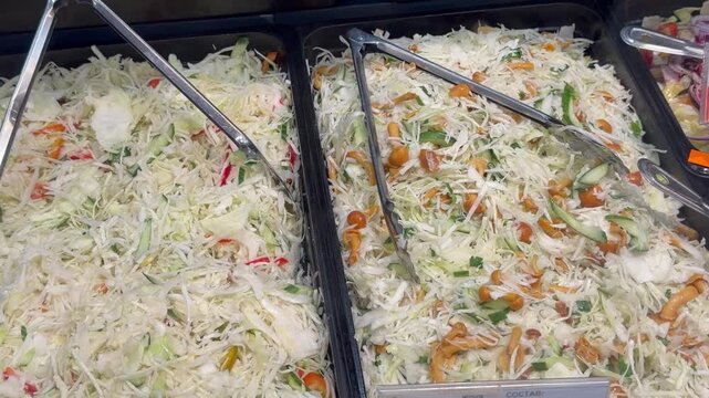 Assortment of fresh cabbage coleslaw salads with cucumbers, red peppers and marinated pholiota mushrooms inside buffet trays. Self service canteen catering food counter layout close up.