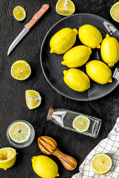 Make lemonade at home. Lemons, juicer, glass and bottle for beverage on black background top view