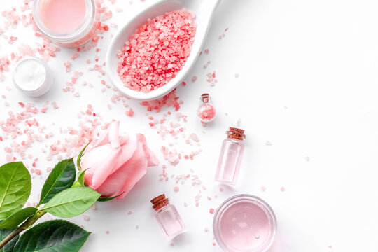 Rose bath salt in spoon near rose petals on white background top view copyspace