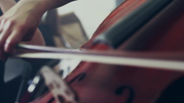 Musician hands bowing cello strings close up. Classical music instrument dark.