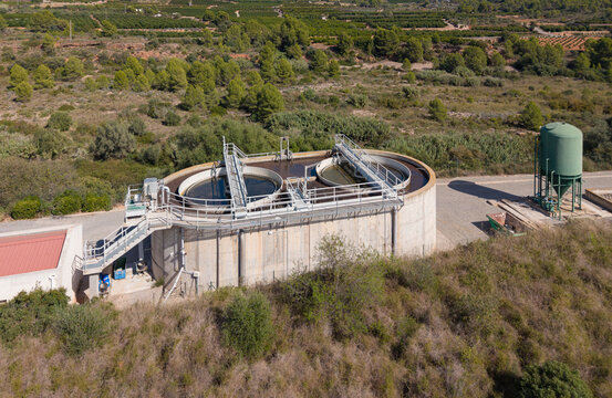 Compact wastewater treatment plant with circular clarifiers and an aeration basin surrounded by dry scrubland and orchards