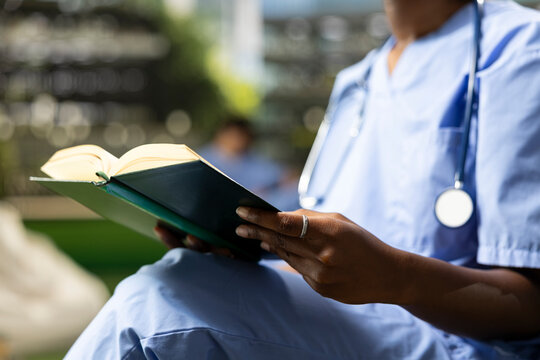 Healthcare, textbook and scrubs as person wearing stethoscope reads open book while seated outdoors. Continuing education, medical knowledge and professional development suggest clinical study.