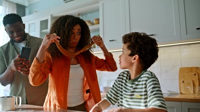 Multiethnic family baking cookies home kitchen. Mother joking dough, boy smiles.