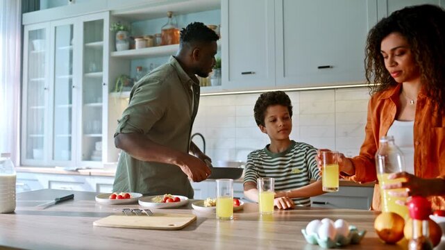 Parents son toasting orange juice glasses kitchen. Happy family breakfast home.