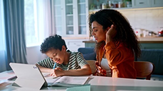 Mother helping son homework kitchen table. Mom explaining lesson tablet home.