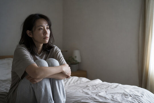 薄暗い寝室で膝を抱えて座る日本人女性