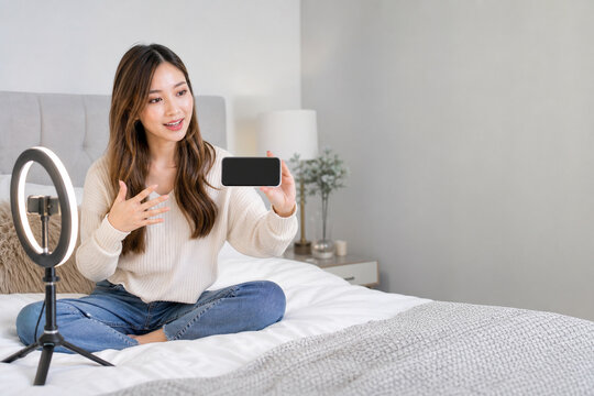 寝室でリングライトを使いスマートフォンに向かって話す日本人女性