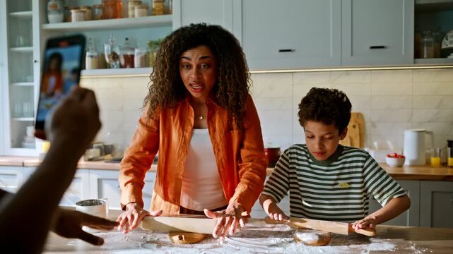 Father filming mother son rolling dough phone. Black family baking home kitchen.