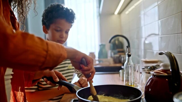 Close up hands stirring omelette frying pan. Single parent cooking son kitchen.