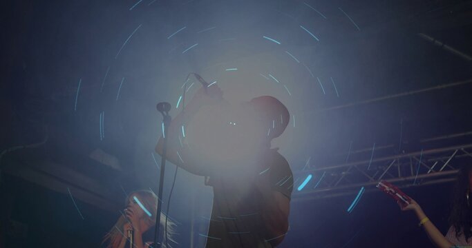 Central vocalist holding microphone cable near face while singing under hazy stage light trails