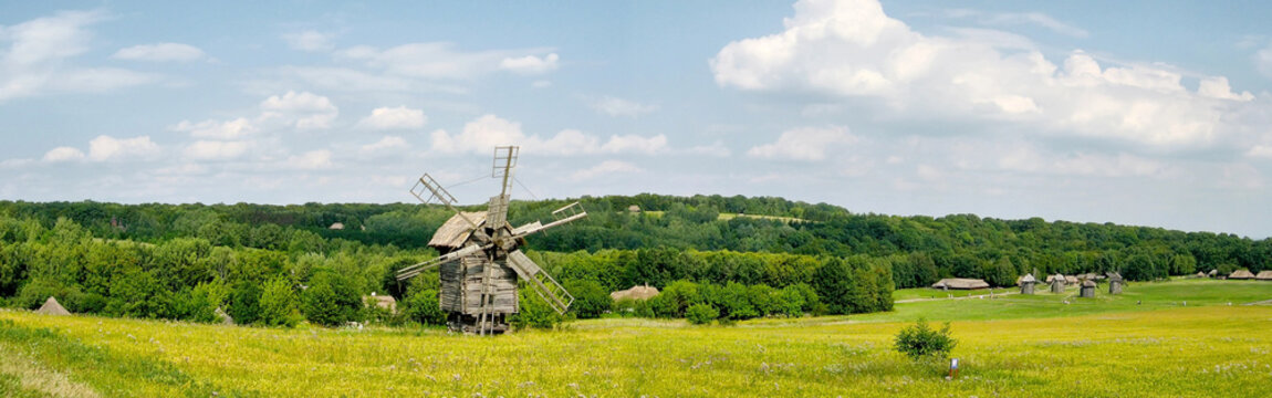 Scenic landscape view of traditional old wooden windmill standing in yellow flower field with green forest under blue sky Pyrohiv in Kyiv