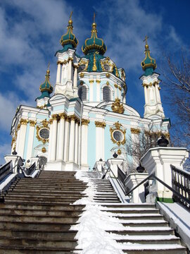Low angle view of beautiful Saint Andrew orthodox church baroque facade with turquoise domes from snowy stone stairs under blue sky in Kyiv