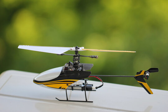 Small black and yellow remote controlled toy helicopter standing on white surface side view 
