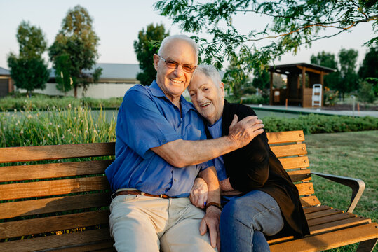 Portrait of a happy elderly retired married couple hugging on a park bench in the afternoon sunlight; Melbourne, Victoria, Australia