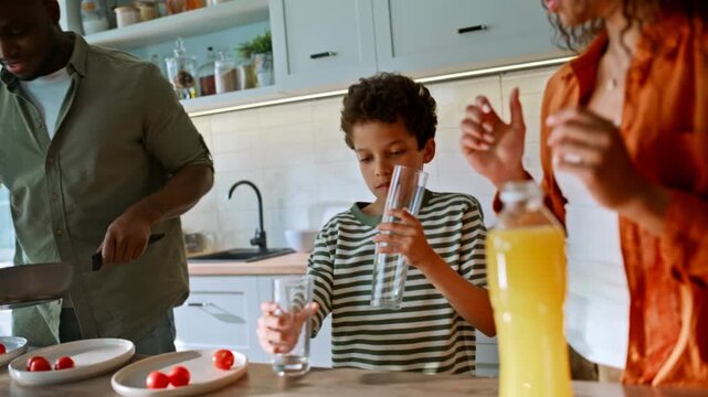Mother pouring orange juice glass son helping. Father cooking eggs home kitchen.